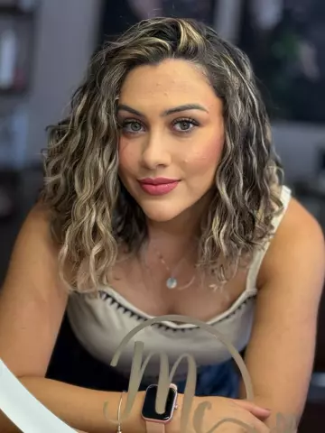 Cliente com cabelo ondulado iluminado, diante do espelho com a logo do studio
